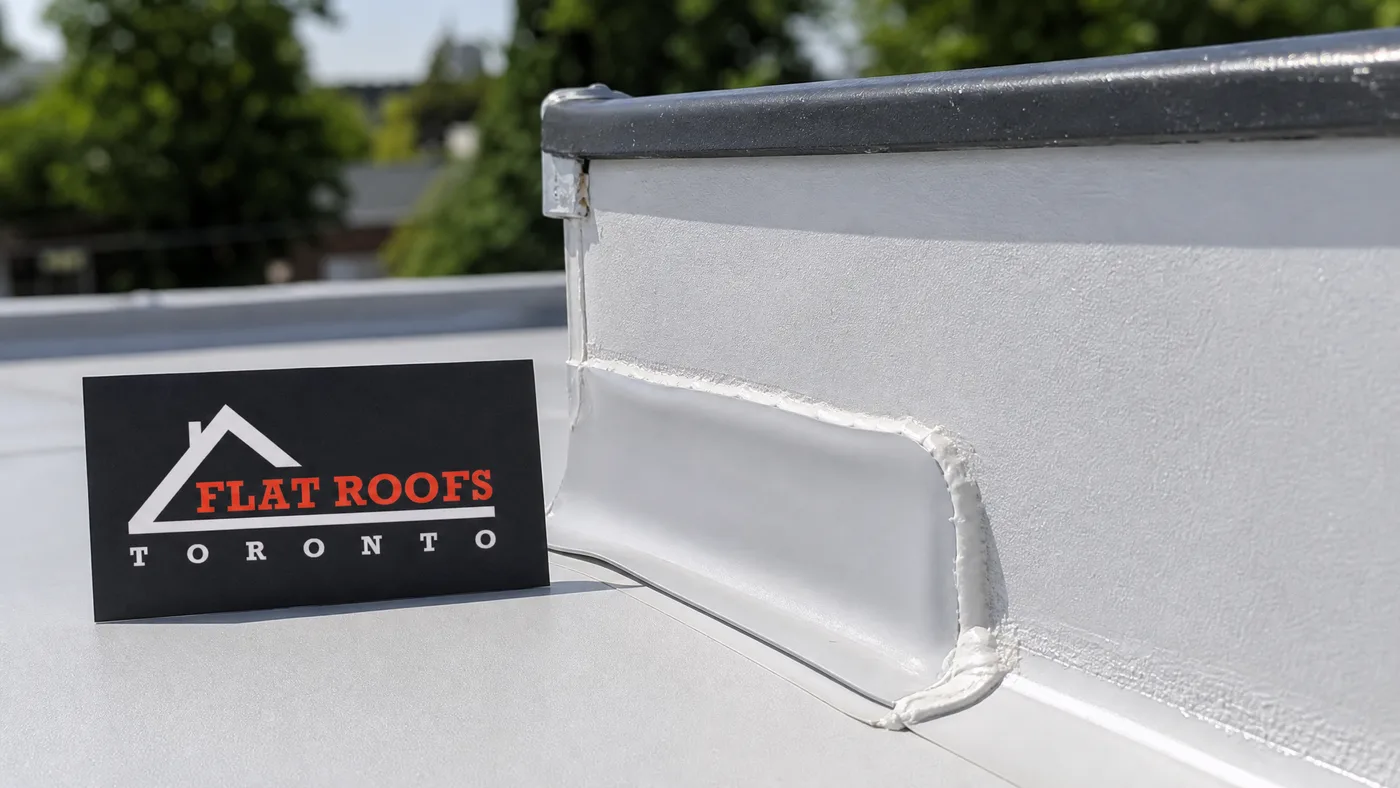Close-up of a low slope roof membrane seam and flashing detail with a small Flat Roofs Toronto sign placard nearby