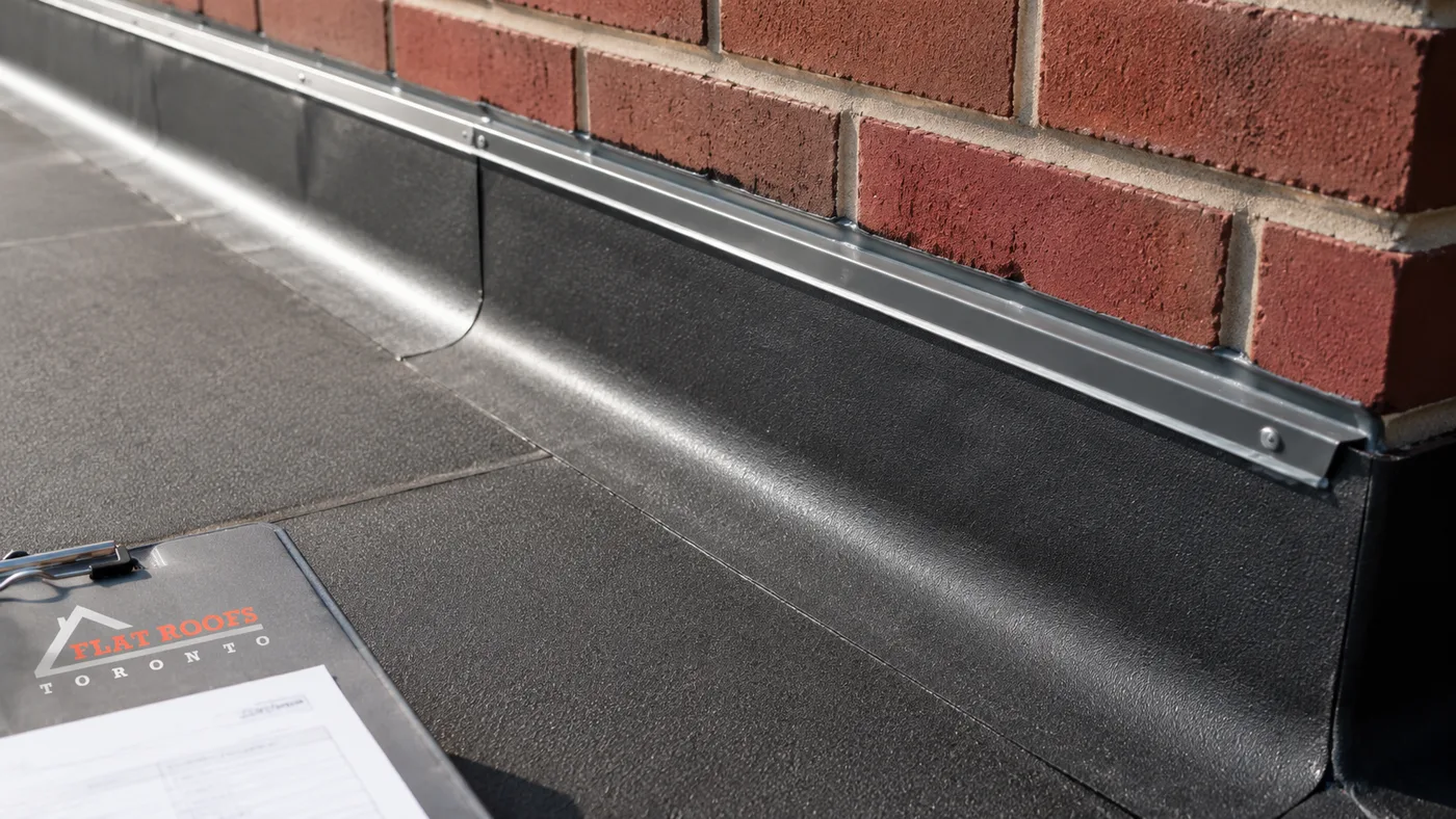 Close-up detail of a completed flat roof repair in Oshawa showing new membrane flashing at a parapet wall junction